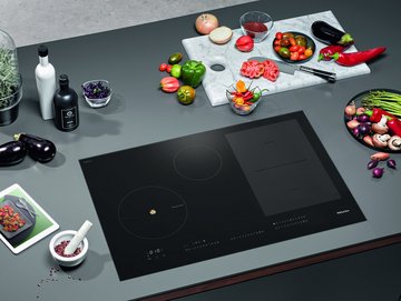 Inductiekookplaat met veel voedsel eromheen plus tablet met Miele CookAssistant-app